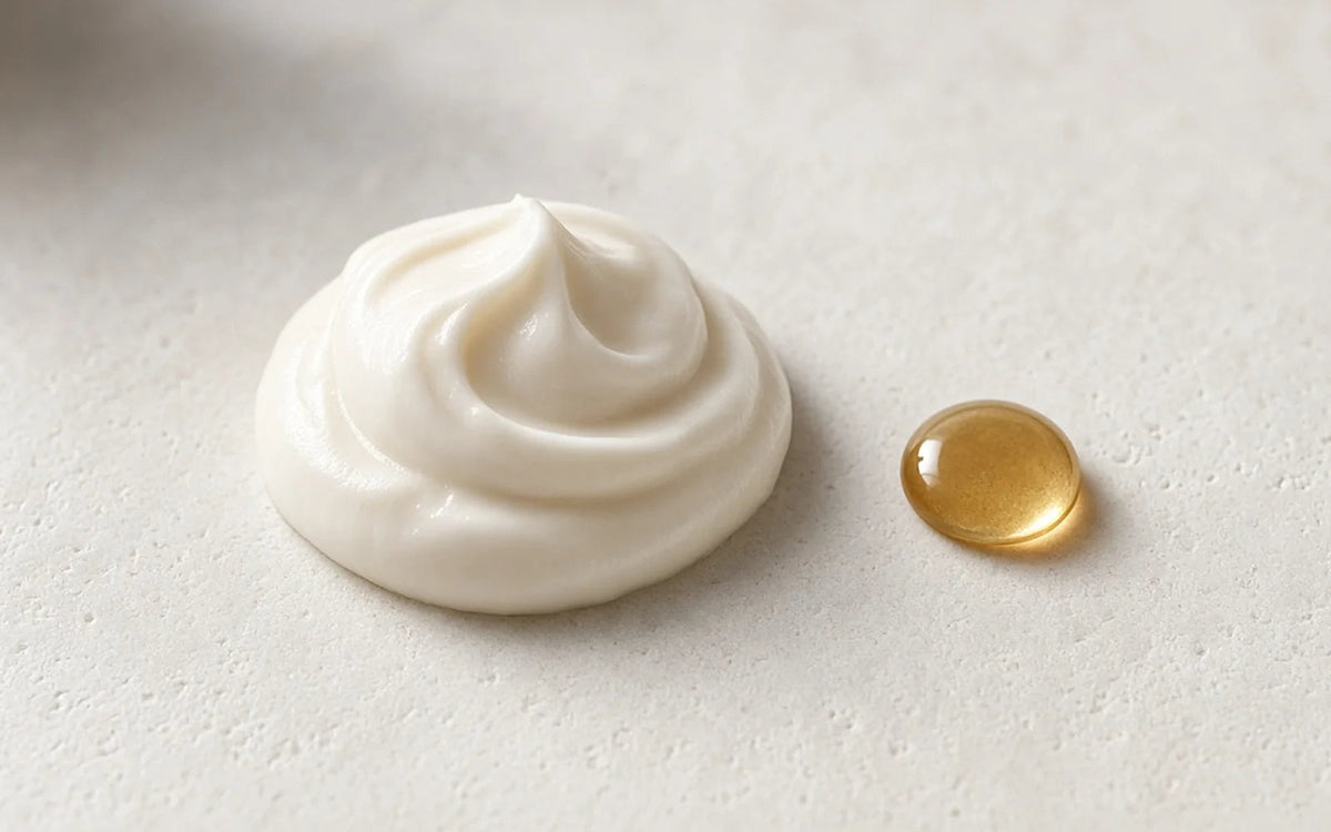 A rich cream texture with a single drop of rose oil on pale stone